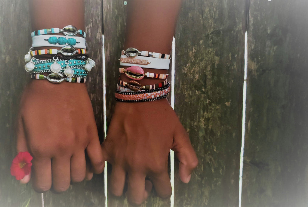 two hands holding together, one hand has multiple bracelets in blush pink colors ,other hand has turquoise color bracelets, fresh water pearls , gemstones.