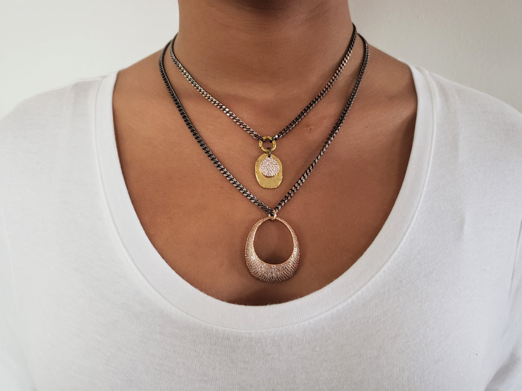 Girl is wearing double chain necklace in antique copper chain.First layer has gold color disc with rose gold micro pave sz pendant.Second layer has large rose gold micro pave sz ellipse pendant.
