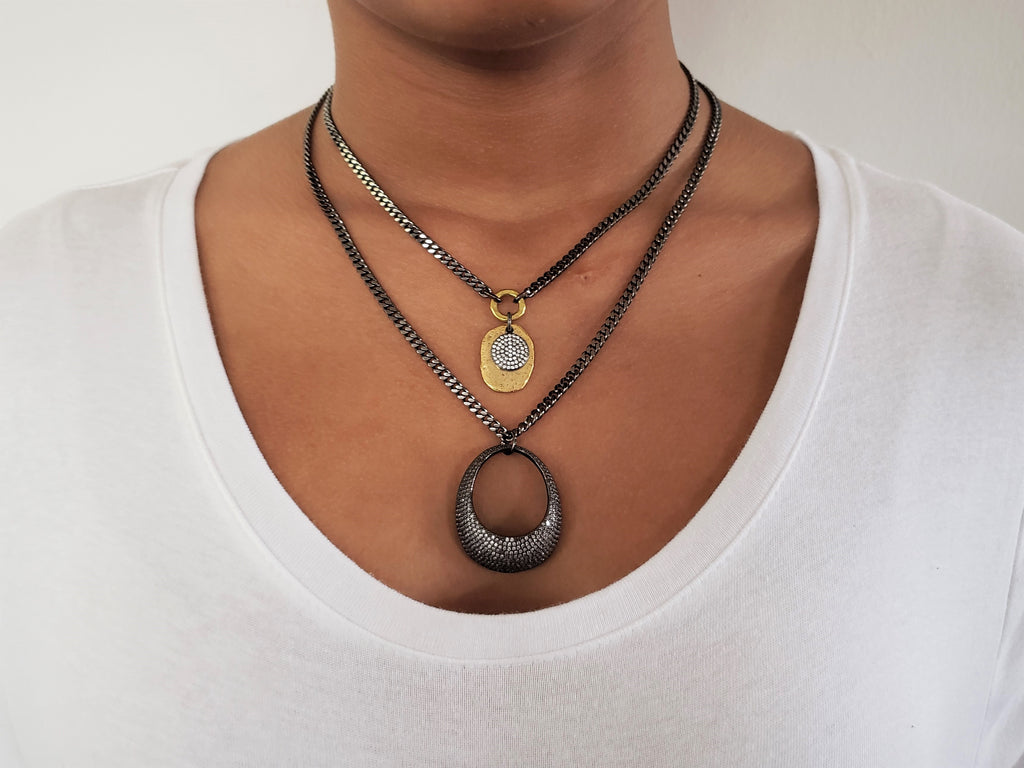 Girl is wearing double chain necklace.First layer has gunmetal chain with gold color disc and black micro pave Sz disc.Second layer has large,gunmetal,crystal micro pave sz ellipse pendant.