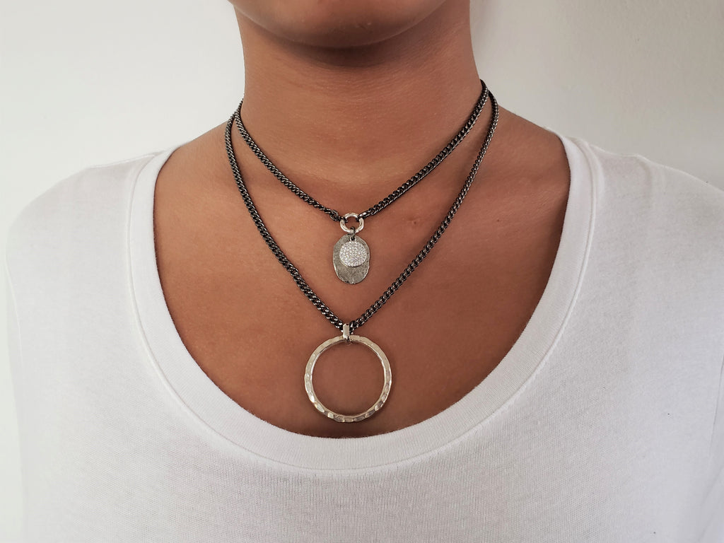 Girl is wearing gunmetal double chain necklace .First layer has silver color disc with gunmetal micro pave sz pendant.Second layer has large sterling silver hammered circle.