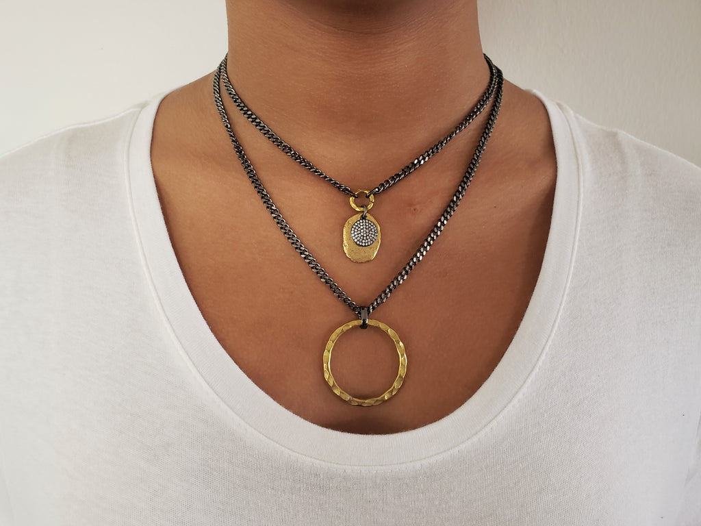 Girl is wearing Double chain necklace.First layer has gray chain with gold color disc and black micro pave Sz disc.Second layer has large,hummered brass circle.