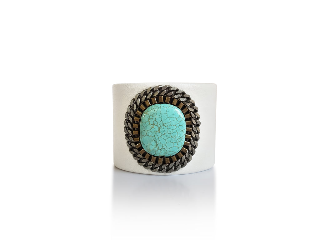 White leather cuff with turquoise stone center piece adorned by brass chains.