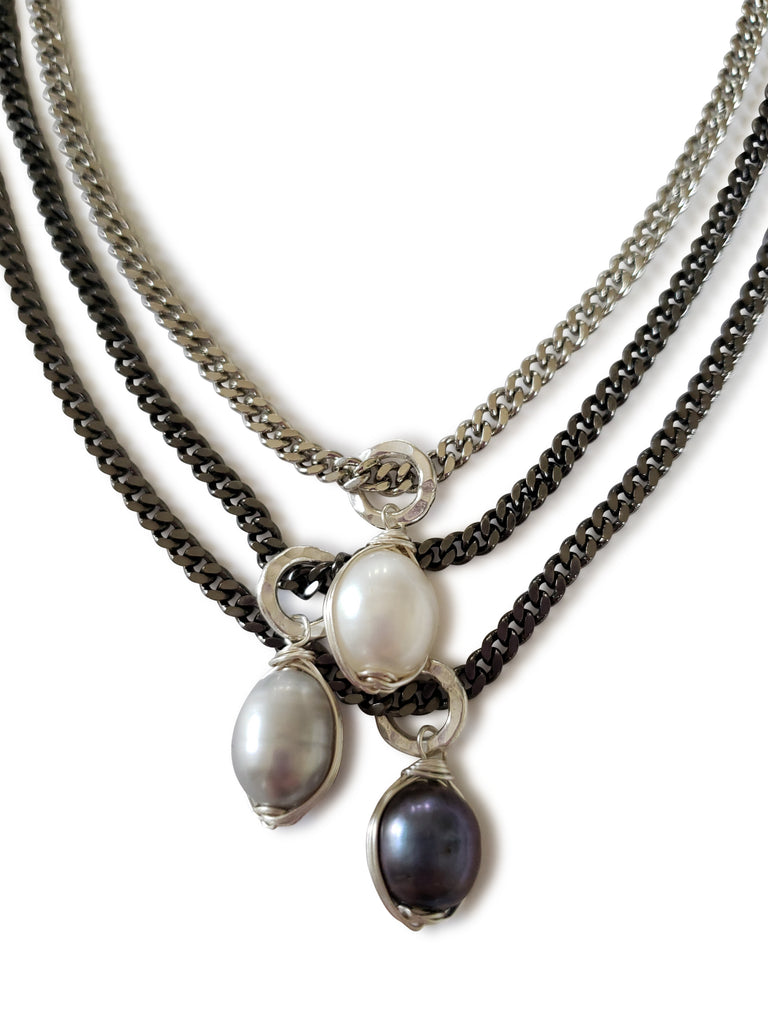 triple chain necklace cose up showing first layer in silver chain and white fresh water pearl wrapped in silver wire as apendant, second layer has gray chain with light gray fresh water pearl wrapped in silver wire as apendant, third layer has gunmetal chain with dark gray fresh water pearl wrapped in silver wire as a pendant.