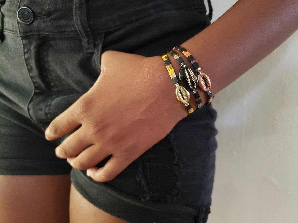 Girl is wearing black shorts , hers hand is in apocket .She has 3 black bead cowrie shell bracelets . Cowrie shells are in black, gold and copper.